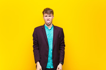 young blonde man feeling disgusted and irritated, sticking tongue out, disliking something nasty...