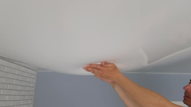 Men hands touch a bubble from a stretch ceiling. Flood, water leakage from the ceiling in the apartment.