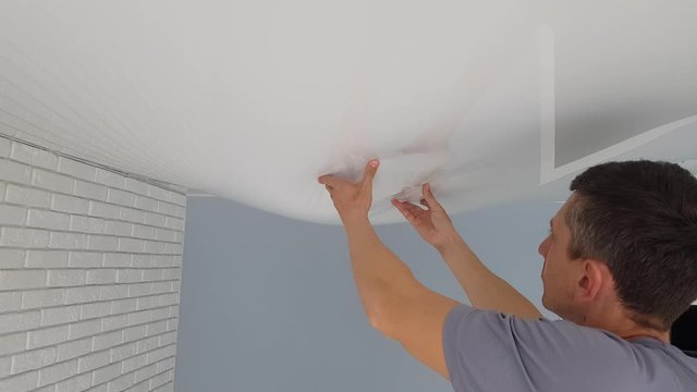 Men is hands hold a bubble from a stretch ceiling.  Flood, water leaks from the ceiling in the apartment.