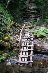 A wooden staircase in the mountains descends to the mountain river from the waterfall.