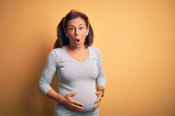Middle age pregnant woman expecting baby at aged pregnancy afraid and shocked with surprise expression, fear and excited face.