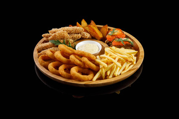 onion rings nuggets french fries ribs potato wedges white sauce on a wooden plate