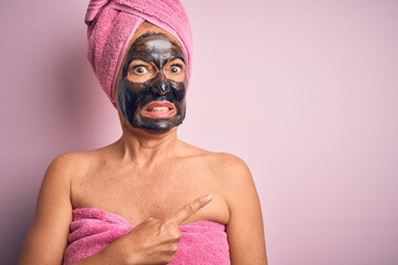 Middle age brunette woman wearing beauty black face mask over isolated pink background Pointing aside worried and nervous with forefinger, concerned and surprised expression