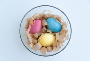 Colorful Easter eggs in a glass bowl with a hay isolated on white background. Top view