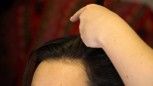 The stylist combs out a lock of hair of a brunette girl