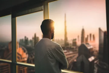 Papier Peint photo Dubai Homme d& 39 affaires arabe regardant à travers le balcon du bureau vu à travers la fenêtre en verre. jeune homme arabe regardant la ville de Dubaï à travers la fenêtre de l& 39 hôtel.