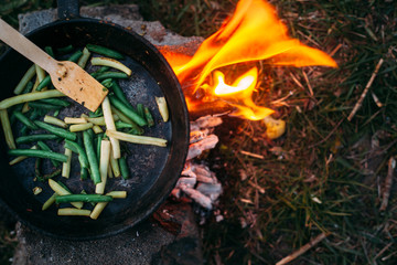 String beans in a pan. Cooking vegetables on an open fire. Food on a camping trip. Wooden spatula in a pan.