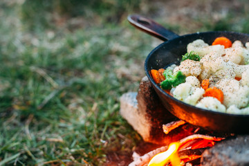 Cauliflower, broccoli and carrot in a pan. Cooking on an open fire. Outdoor food. Grilled vegetables. Food on a camping trip.