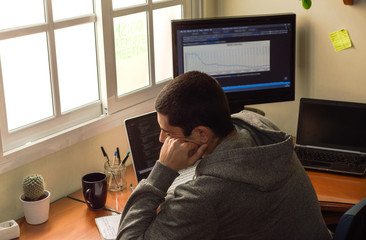 Bored and disinterested young man working from home. Small office at home to telework. Concept of telecommuting or teleworking.