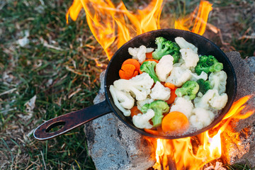 Cauliflower, broccoli and carrot in a pan. Cooking on an open fire. Outdoor food. Grilled vegetables. Food on a camping trip.