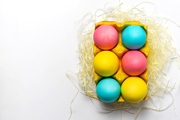 Colored eggs in yellow paper egg tray isolated on white background. Easter postcard design idea. Top view, close-up, copy space