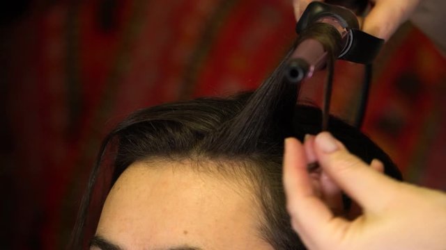 The stylist curls a strand of hair winding her hair on a hot Curling iron
