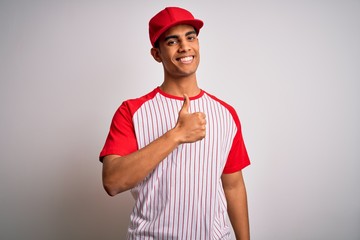 Young handsome african american sportsman wearing striped baseball t-shirt and cap doing happy thumbs up gesture with hand. Approving expression looking at the camera showing success.