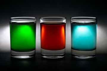 three glowing shot glasses with colorful drinks