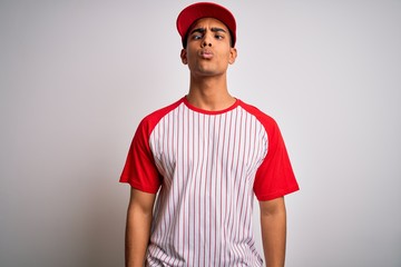 Young handsome african american sportsman wearing striped baseball t-shirt and cap making fish face with lips, crazy and comical gesture. Funny expression.