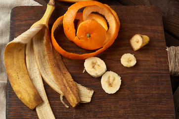 banana and orange skins on a brown wooden board