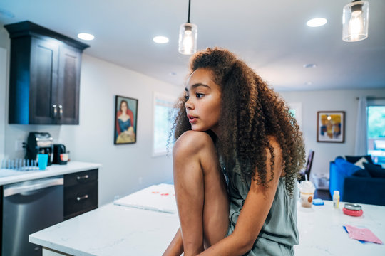 Girl sitting on kitchen counter looking bored, resting chin on knee