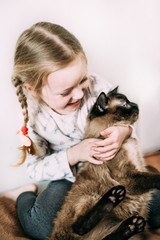 A little girl laughs and plays with her beloved pet. Siamese beautiful and very patient cat. Children and animals. Happiness in the family. Family atmosphere. Without a cat life is not good
