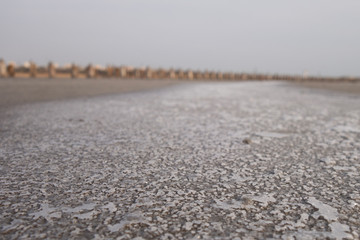 Fototapeta na wymiar Sandy bottom of a dried reservoir with cracks and salt crystals.