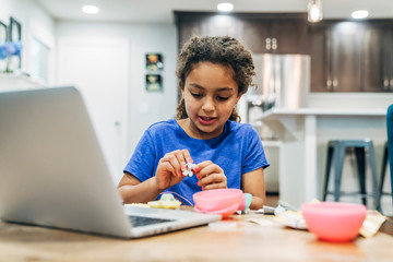Girl building toy using online video tutorial on laptop computer