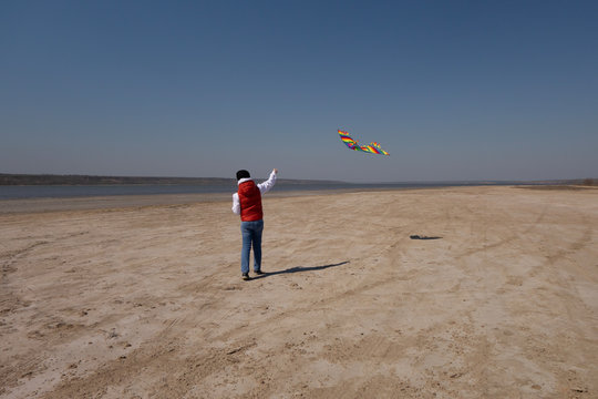 A 10 Year Old Boy In A White Sweatshirt And Orange Vest Launches A Kite On A Deserted Beach In Solitude.