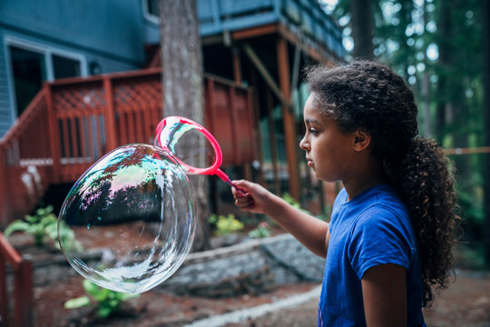 Girl blowing giant bubbles in the back yard of house