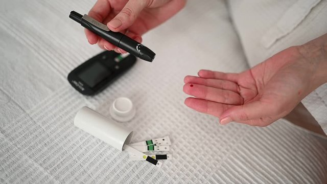 Diabetes checking blood sugar level. Woman using lancelet and digital glucometer at home. Medicine, diet diabetes, health care concept - female hands with glucometer checking body glucose level