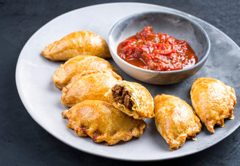 Traditionelle südamerikanische Empanada de Carne angeboten mit Chili Sip als closeup auf einem Modern Design Teller
