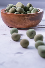 Wasabi peanuts in a wooden bowl on white textured background. Asian snack. Vertical picture.