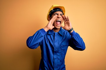 Young handsome african american worker man wearing blue uniform and security helmet Shouting angry out loud with hands over mouth