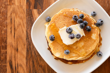 Top angle view on white plate on the wooden board table with pancakes and butter blueberries over and maple syrup or honey
