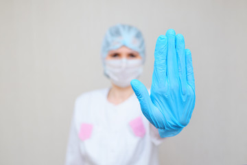 a woman doctor or nurse shows a gloved hand in a stop gesture.