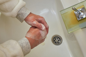 Foamy hands while washing over a sink in a bathroom