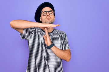 Handsome man with blue eyes wearing striped t-shirt and french beret over purple background Doing...
