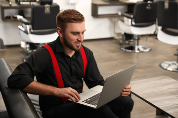 Young business owner working with laptop in barber shop