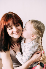 A little blond child gently hugs his brunette mom with handles and kisses her cheek. Joyful mom...