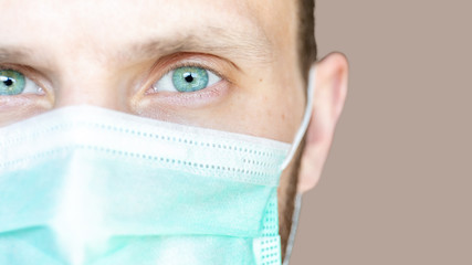 super close-up of a man's face with green eyes in a medical mask, copy space