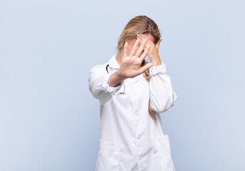 young pretty latin woman covering face with hand and putting other hand up front to stop camera,...