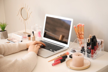 Makeup artist at table with modern laptop and cosmetics