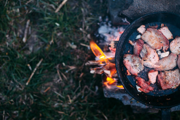 Slices of fried bacon in a pan. Food in a forest camp. Cooking on fire. Picnic in the nature. Grilled food on nature.