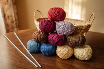 Multi-colored balls of wool yarn folded into a pyramid on a wooden table with knitting needles