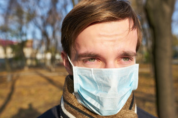 Portrait of young man with medical face mask stands at city street. Guy wearing protective mask from virus outdoor in the people crowdy.