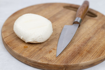 Mozarella cheese on the cutting wooden board with knife