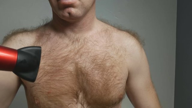 a young, handsome man with a bare torso and raised hairline dries his chest hair with a hair dryer. His body hair is red. a man is sexy. 4K