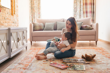 Young beautiful mother plays with her son in a sunny room. Silit with a child on the floor on the...