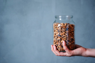 Hands holding a large glass jar with raw beans on a gray background on the left - an empty place...