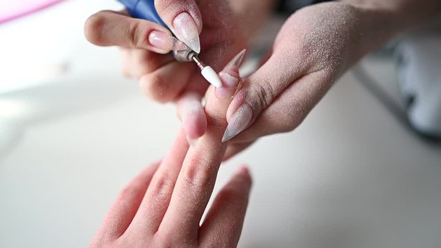 Hardware professional manicure process, cleaning of nails by a milling cutter. Close up female hands in beauty salon. Finger nail treatment, making process. Electric nail file drill in action