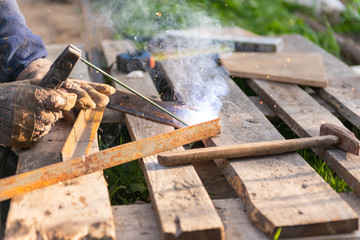 Welding iron. The worker welds the iron parts. Workplace on a pallet with tools.