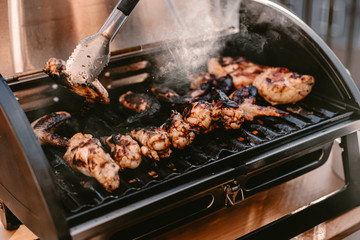 Grill season outdoor in park or balcony. Spring summer grilling. Balcony gas grill. Barbeque fourth of July weekend. Chicken wings on grill. Flame and smoke over grill. BBQ quarantine on balcony.