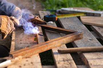 Welding iron. The worker welds the iron parts. Workplace on a pallet with tools.